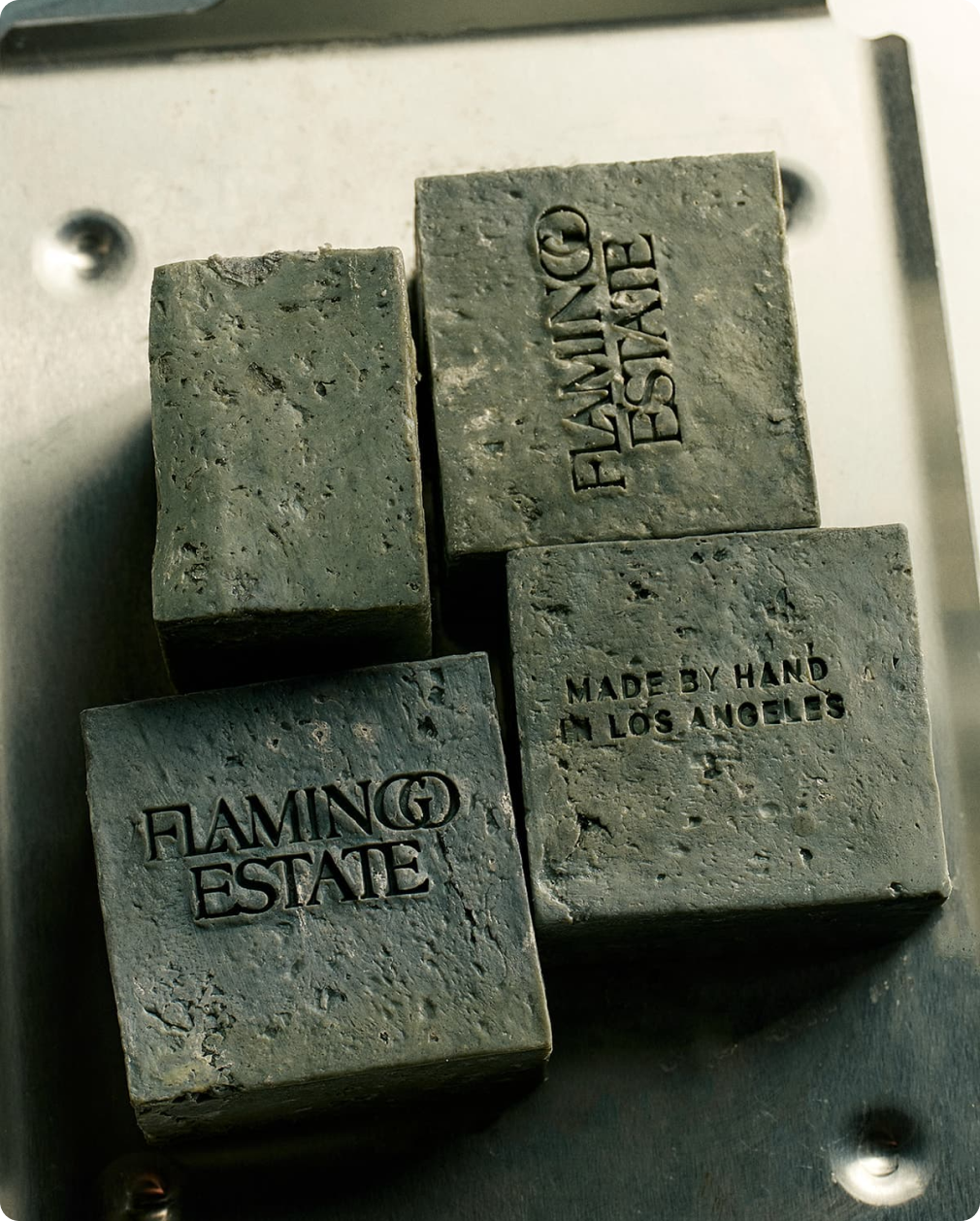 Soap bars imprinted with "FLAMINGO ESTATE" are stacked on a metal tray.