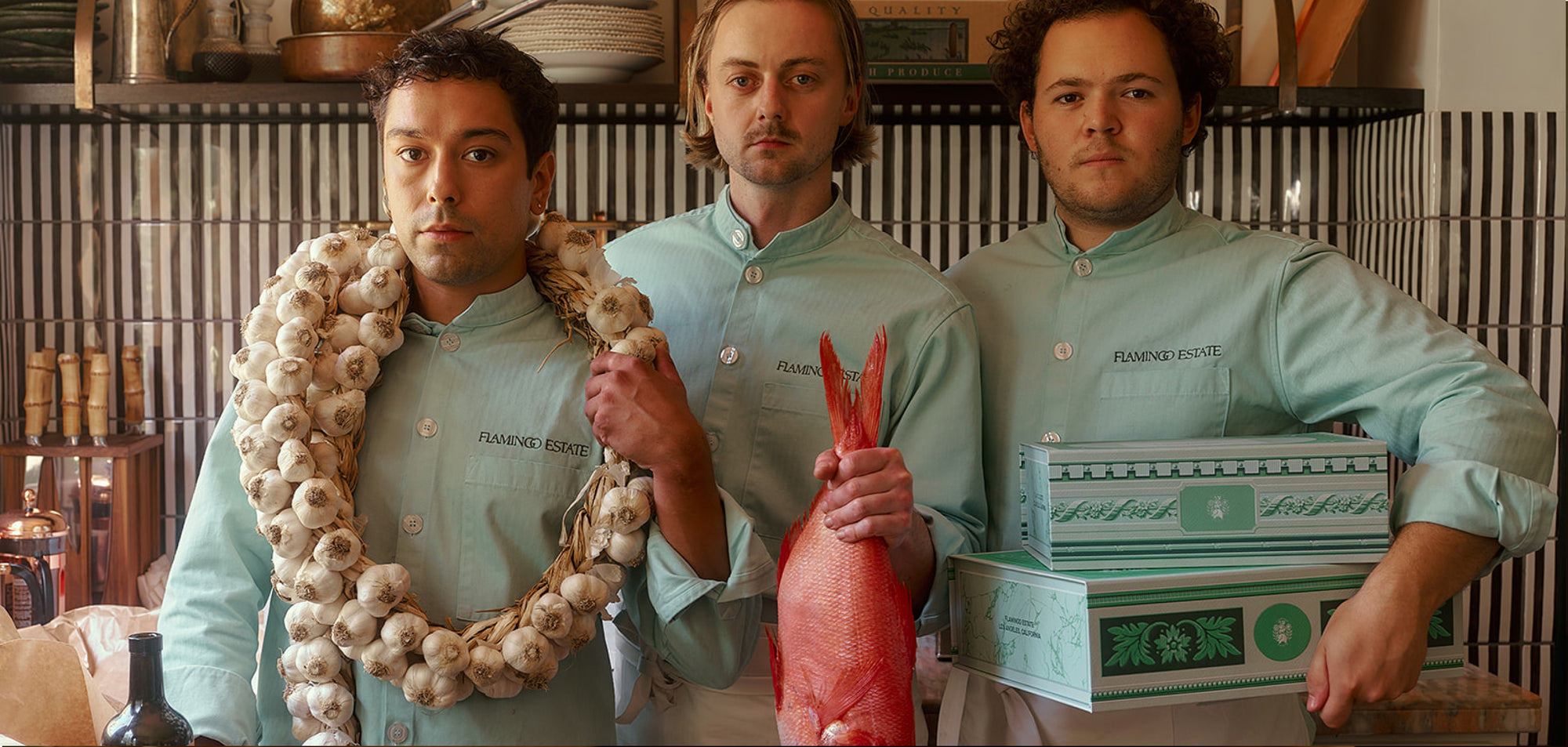 Three individuals in matching light-green shirts stand in a kitchen.