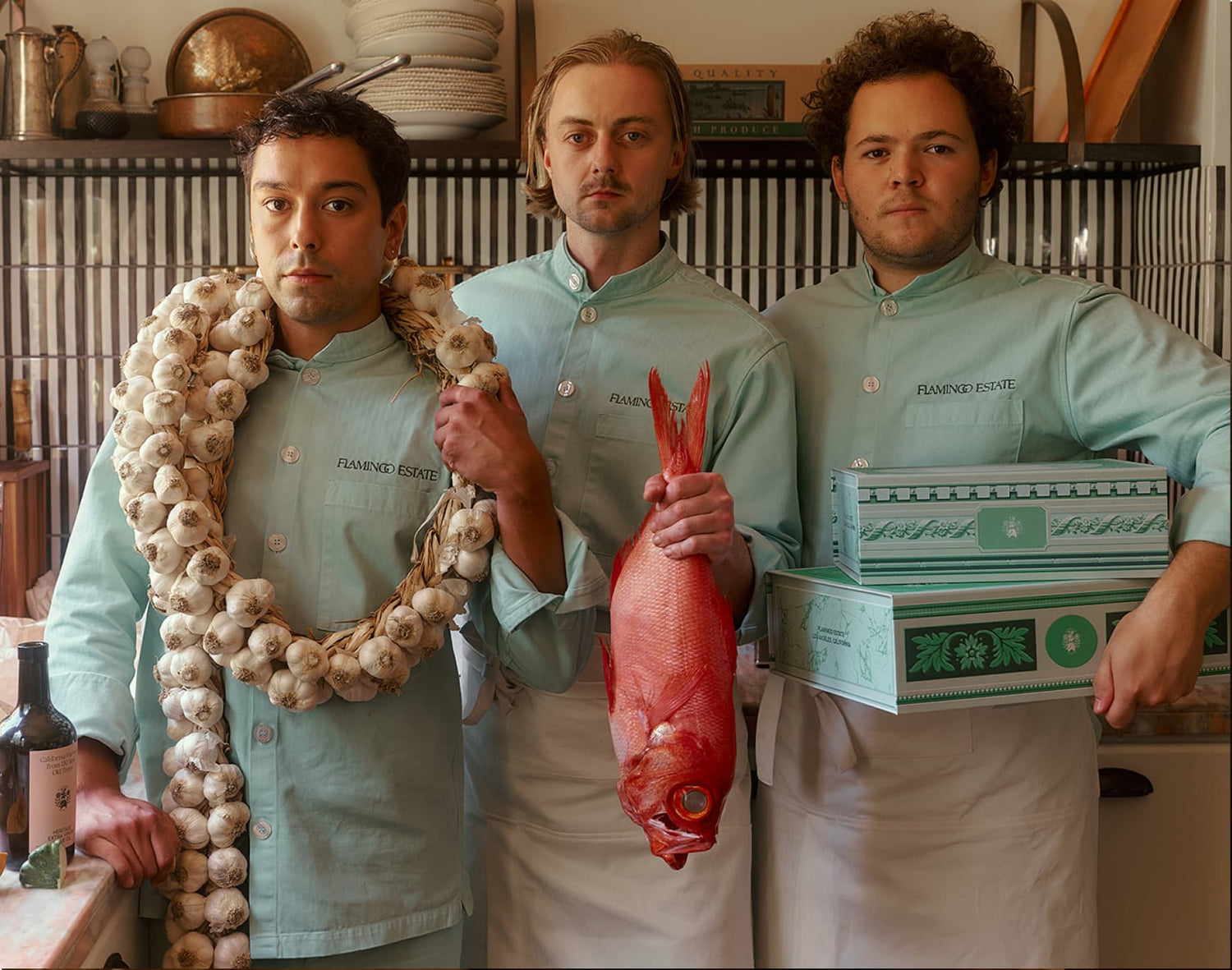 Three individuals in matching light-green shirts stand in a kitchen.