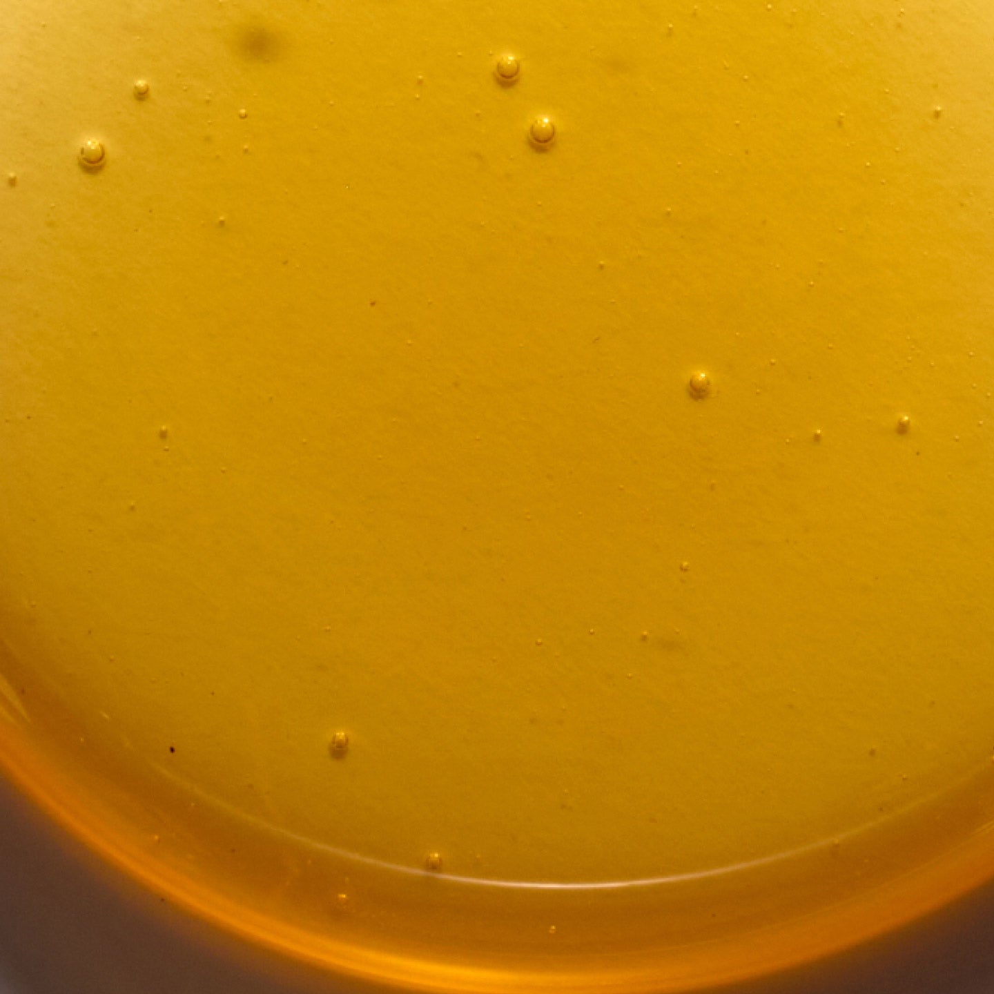 Golden liquid with small bubbles suspended, resting in a round, smooth container.