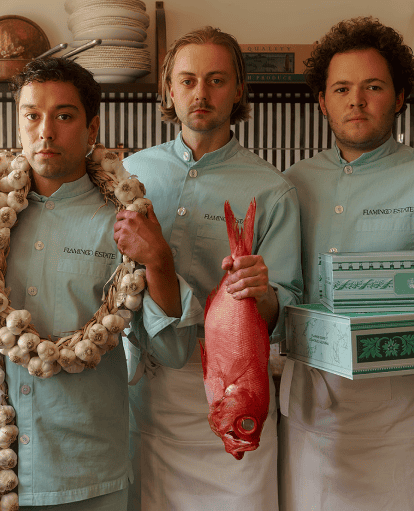 Three individuals in matching light-green shirts stand in a kitchen.