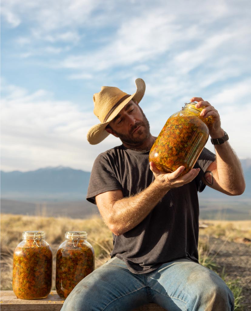 A man wearing a straw hat examines a large jar of preserved vegetables.