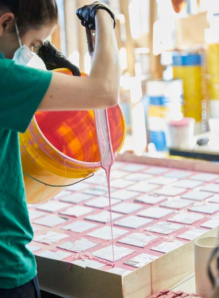 A person in a green shirt pours pink liquid from an orange bucket onto a rectangular surface.