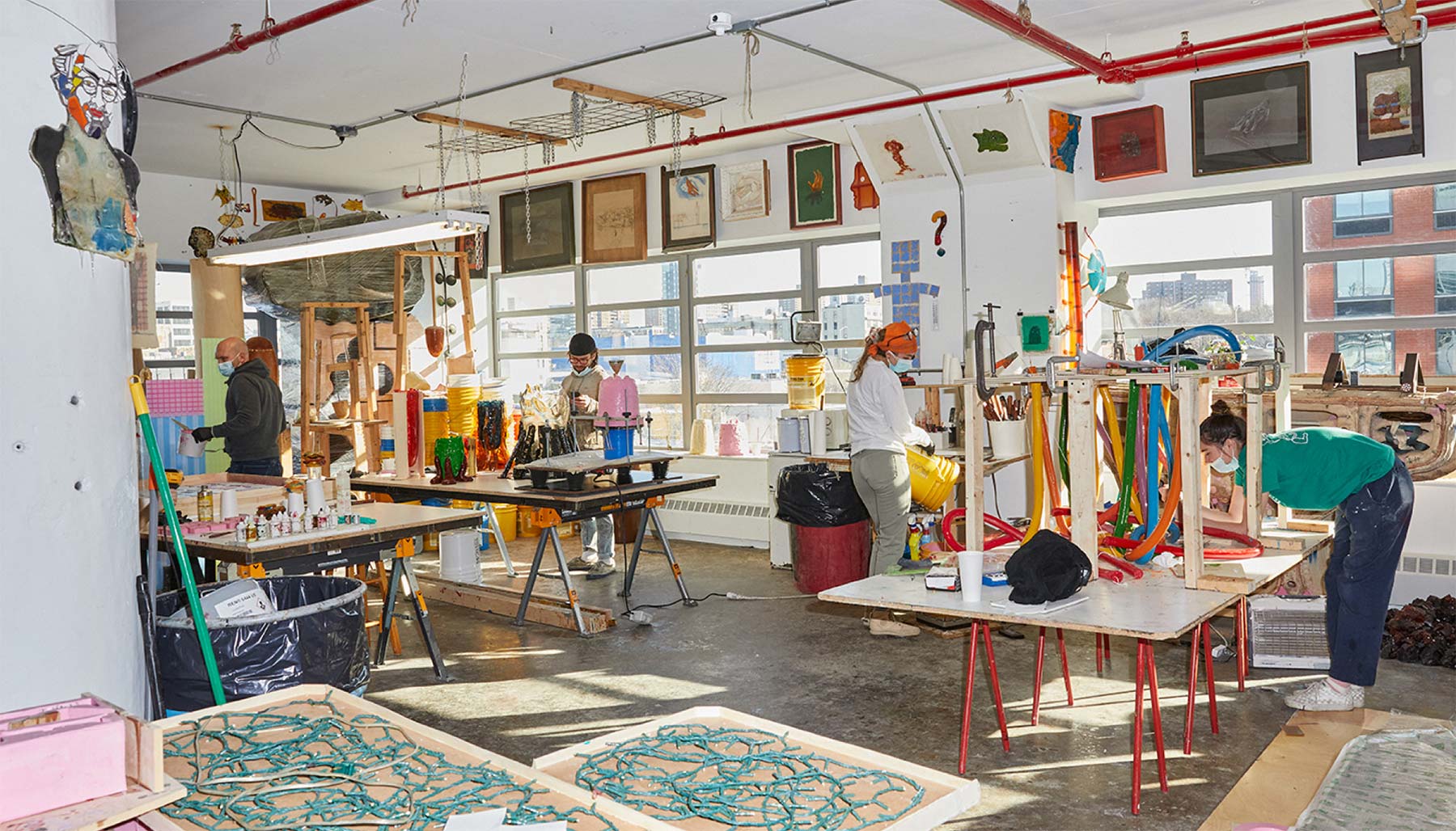 Artists work on colorful sculptures and paintings in a cluttered studio.